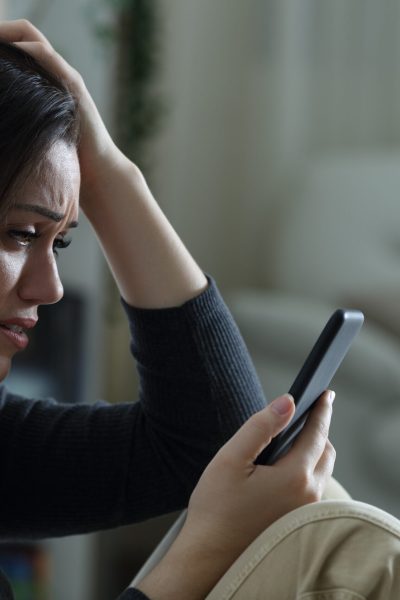 Sad woman reading bad news on mobile phone complaining at home in the night